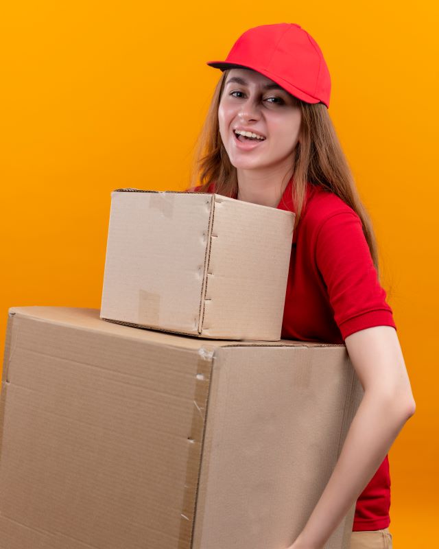 https://www.newcablojistik.com/wp-content/uploads/2023/08/joyful-young-delivery-girl-red-uniform-holding-boxes-isolated-orange-space-1.jpg
